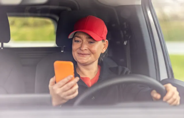 Woman sitting in her stationary car, smiling at her phone, using the Circle K app