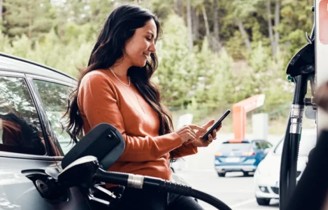 woman leaning against her car while fueling