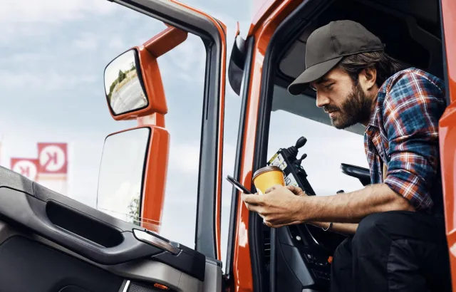Man sitting in his truck with a coffee, checking his phone